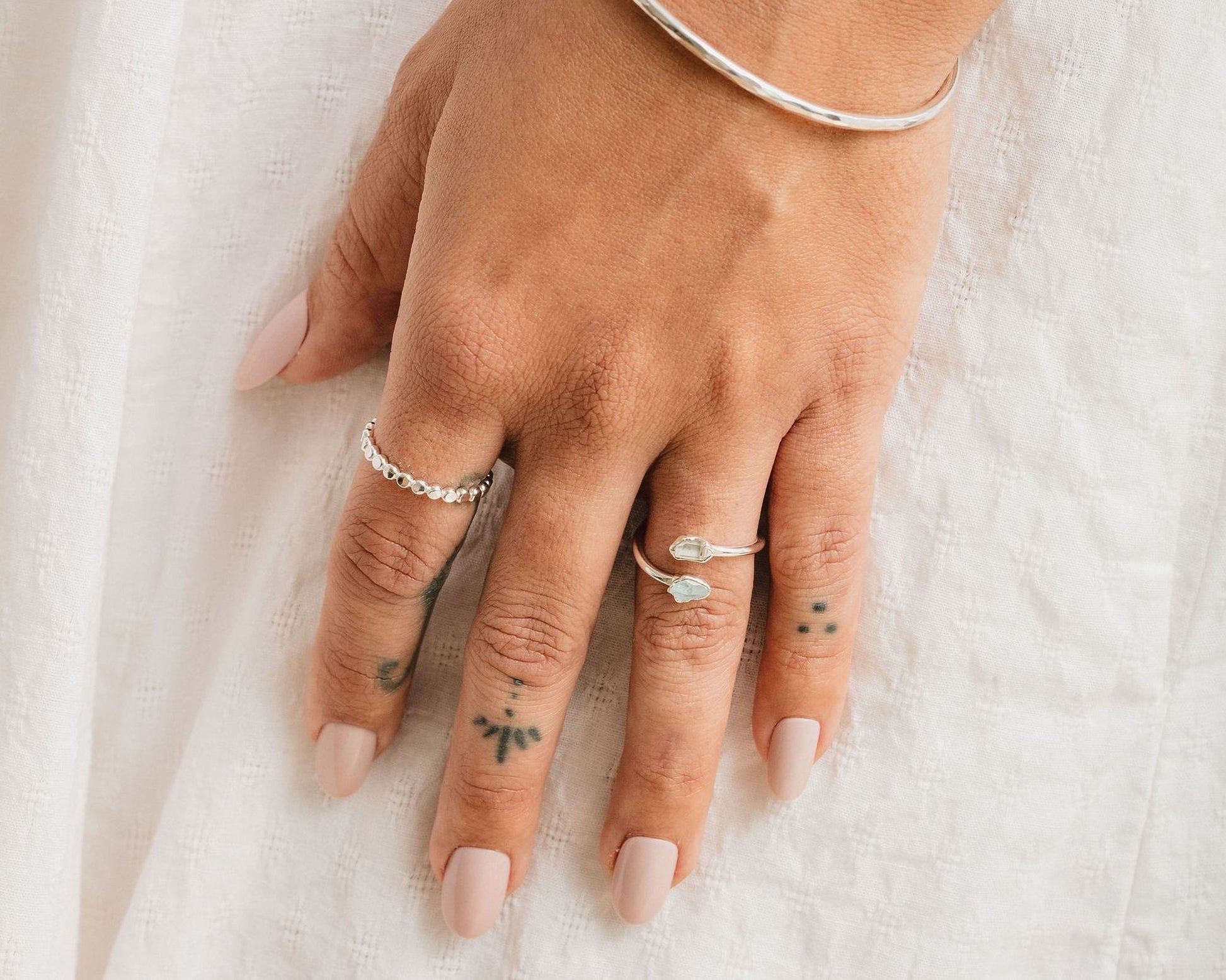 A close-up view of a person's hand adorned with multiple rings and tattoos on the fingers.