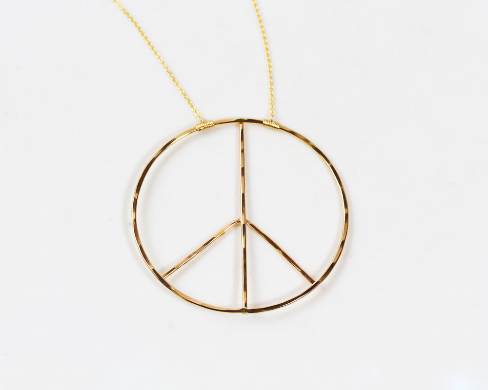 Image shows close up of our Inner Peace Necklace in 14 karat yellow gold filled. This powerful peace sign necklace tells a story as you wear it. Handcrafted from start to finish, this chic statement necklace is offered in sterling silver or gold fill