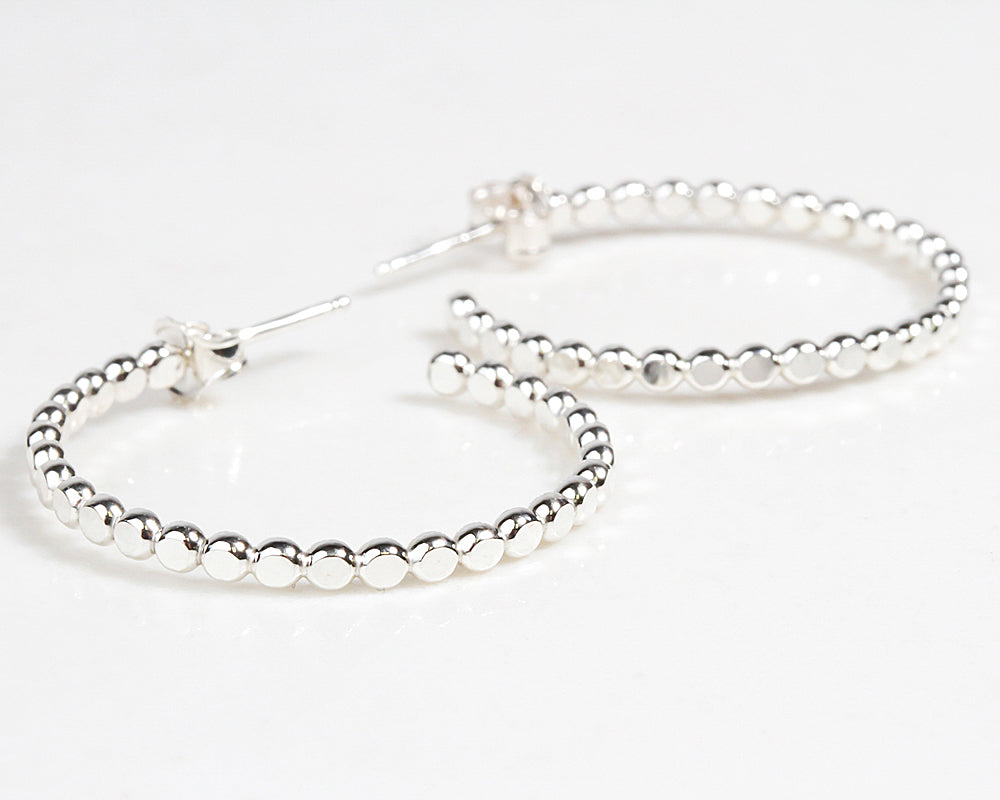 These graceful hoop earrings are handcrafted from hammered bead wire. This material glints and gleams from all angles. Shown here in sterling, our Beaded Ivy Hoop Earrings will quickly become a daily staple. Offered in three sizes and two metals.