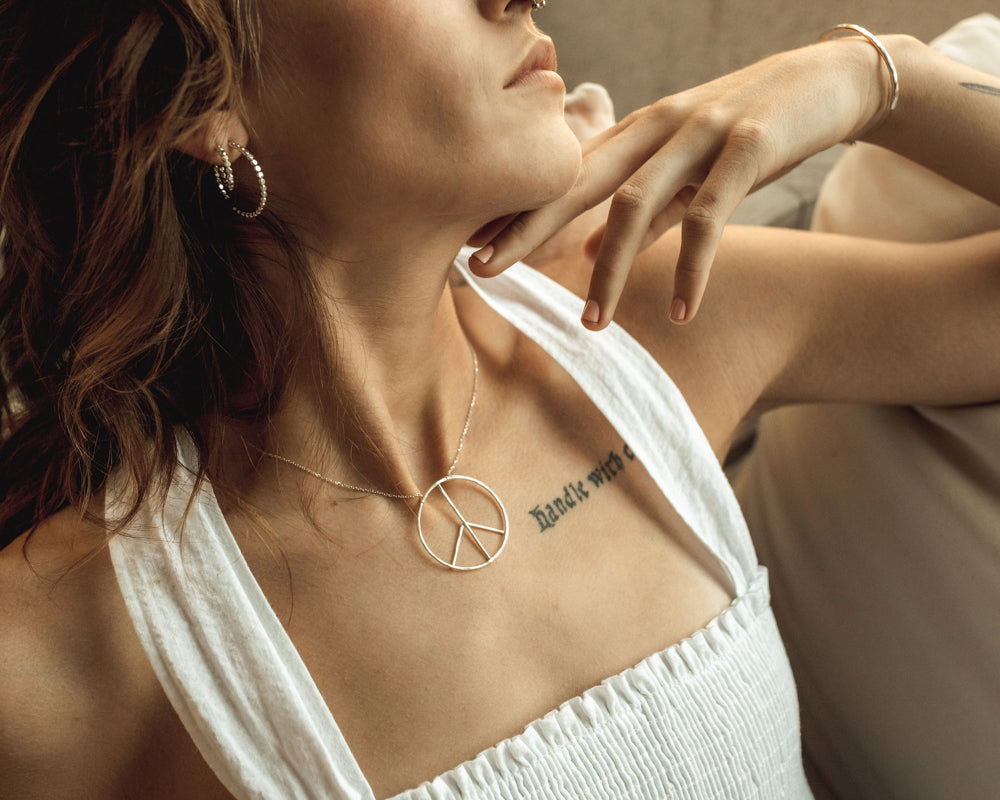 Image shows model wearing the small sterling silver inner peace necklace. Our Inner Peace Sign Necklace carries a powerful message and delivers it in a chic package. Have your Inner Peace Necklace handcrafted in Sterling or 14 karat Gold Filled.