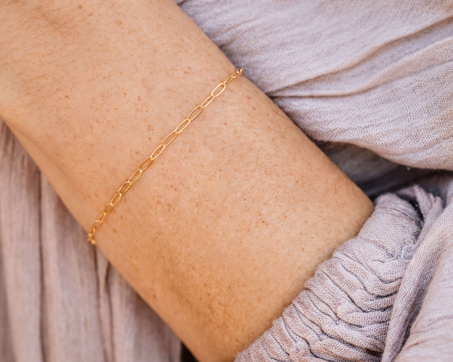 A close-up view of a person's arm wearing a delicate gold chain bracelet.