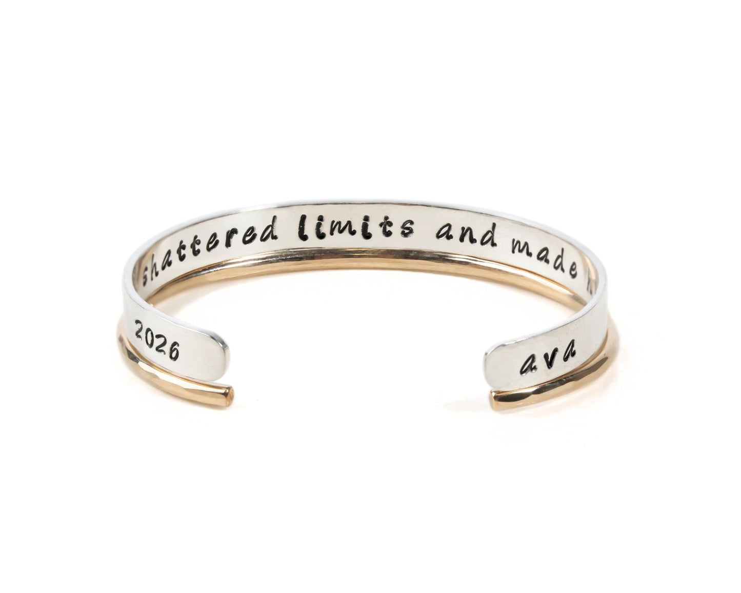 A silver bracelet with the text " Shattered Limits and Made" engraved on it.