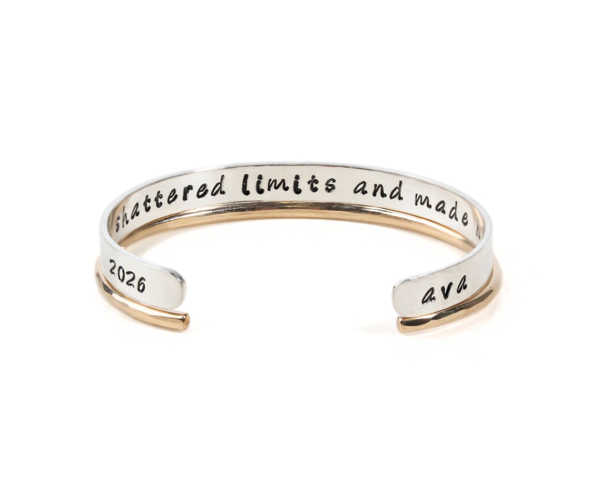 A silver bracelet with the text " Shattered Limits and Made" engraved on it.