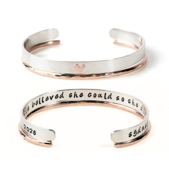 two silver-colored bracelets with a heart-shaped charm on the top. The text on the bracelets reads "She believed she could so she tried and failed and tried again."