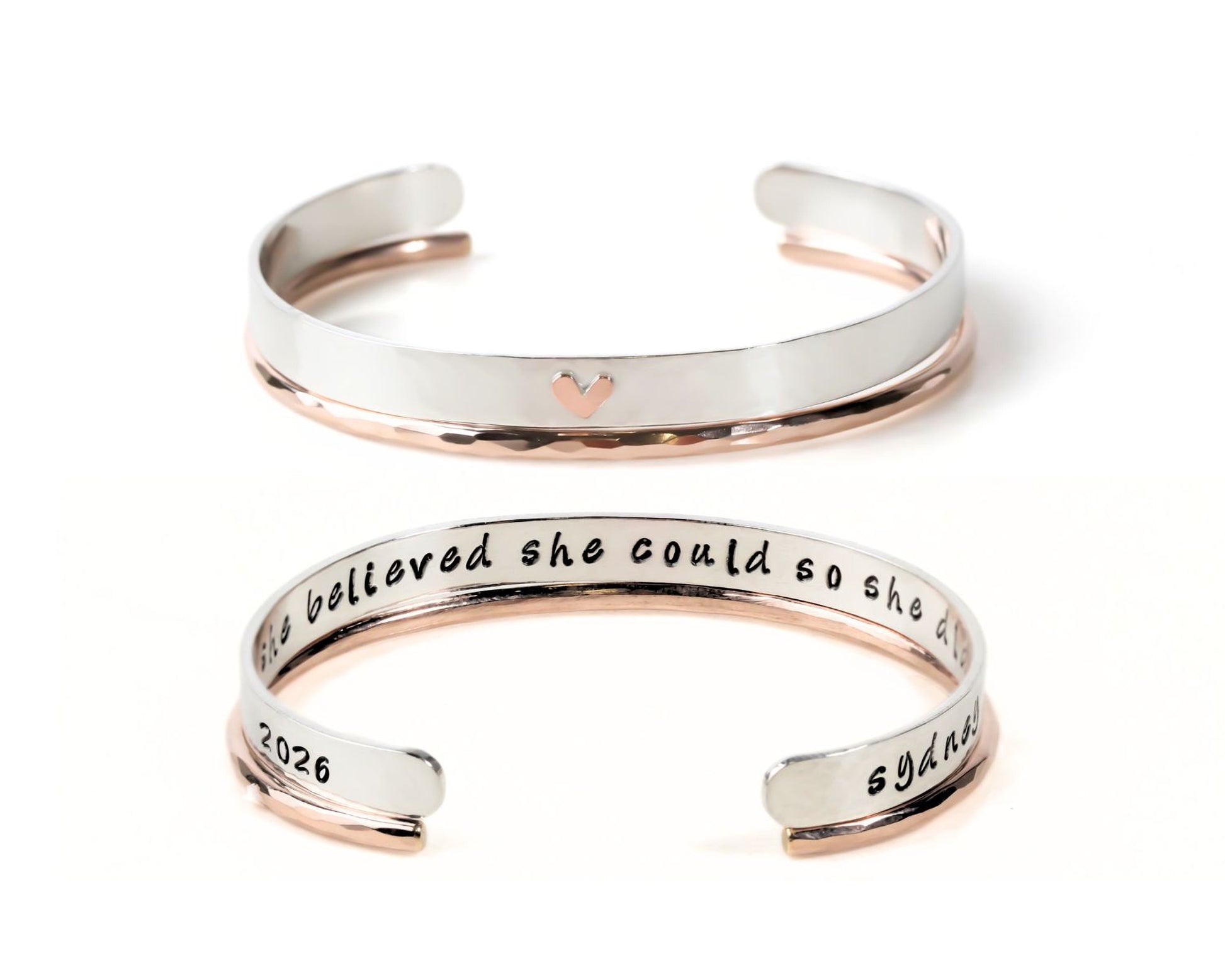 two silver-colored bracelets with a heart-shaped charm on the top. The text on the bracelets reads "She believed she could so she tried and failed and tried again."