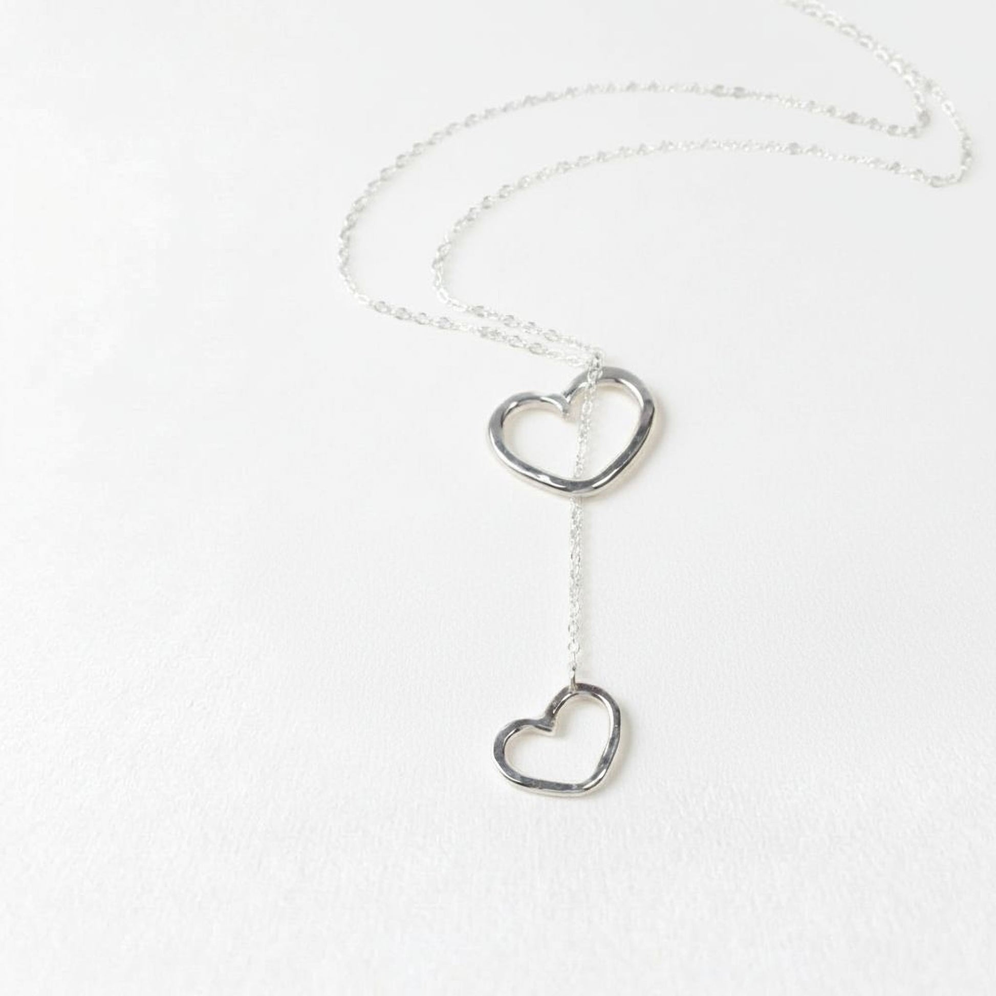 A silver necklace with two heart-shaped pendants hanging from a chain.
