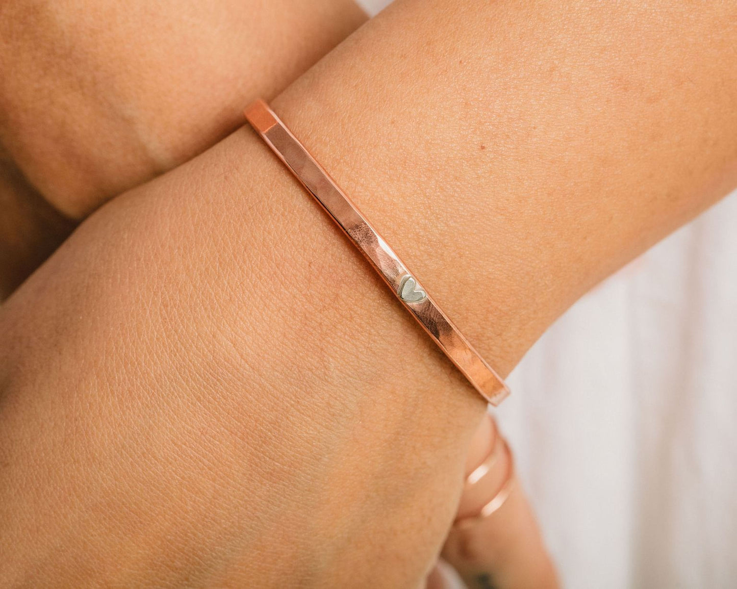 A close-up view of a person's wrist wearing a copper-colored bracelet with a heart-shaped charm.
