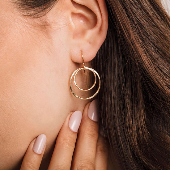 A close-up of a woman's ear with a gold hoop earring featuring two concentric circles.