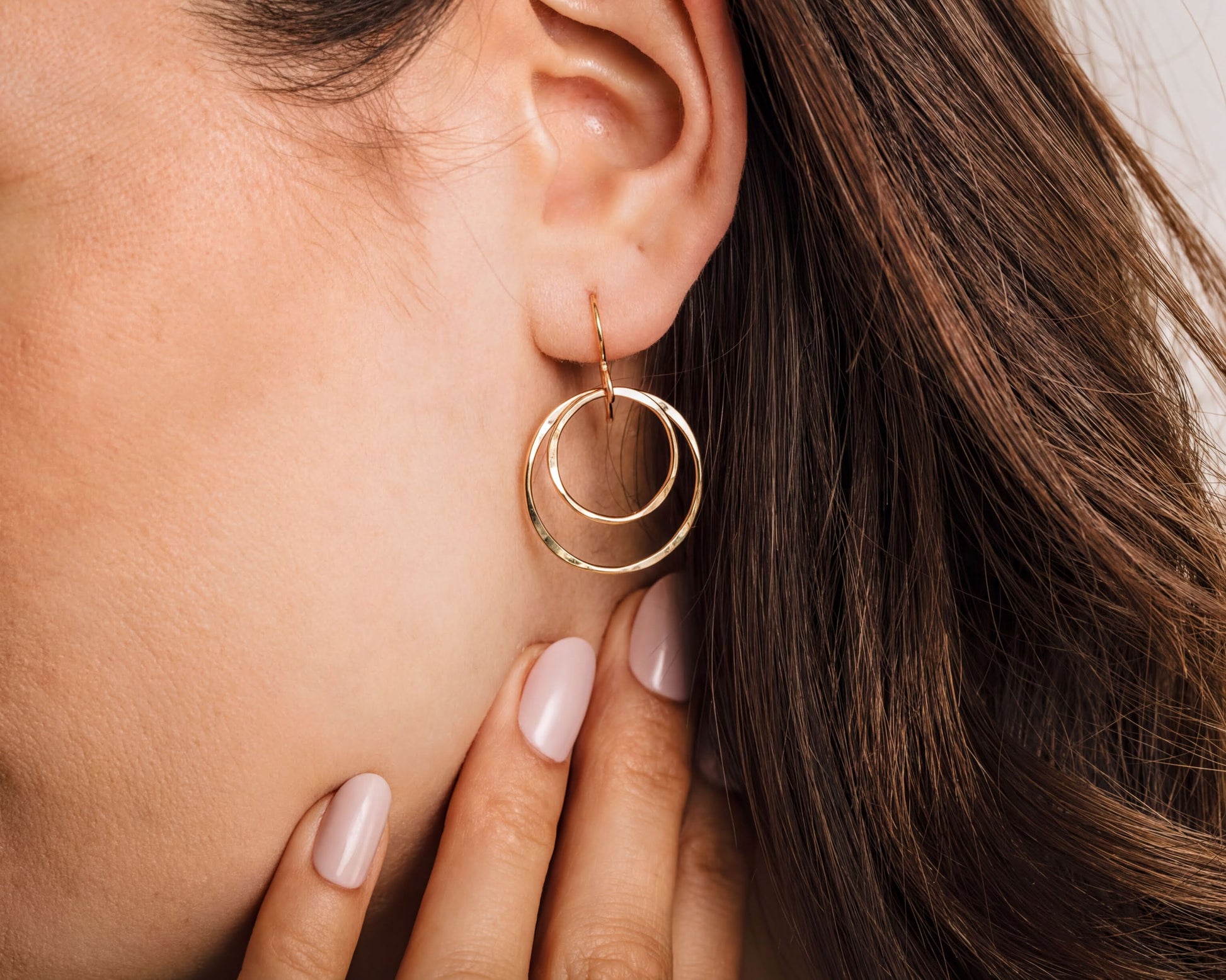 A close-up of a woman's ear with a gold hoop earring featuring two concentric circles.