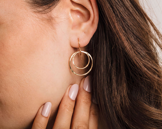 A close-up of a woman's ear with a gold hoop earring featuring two concentric circles.