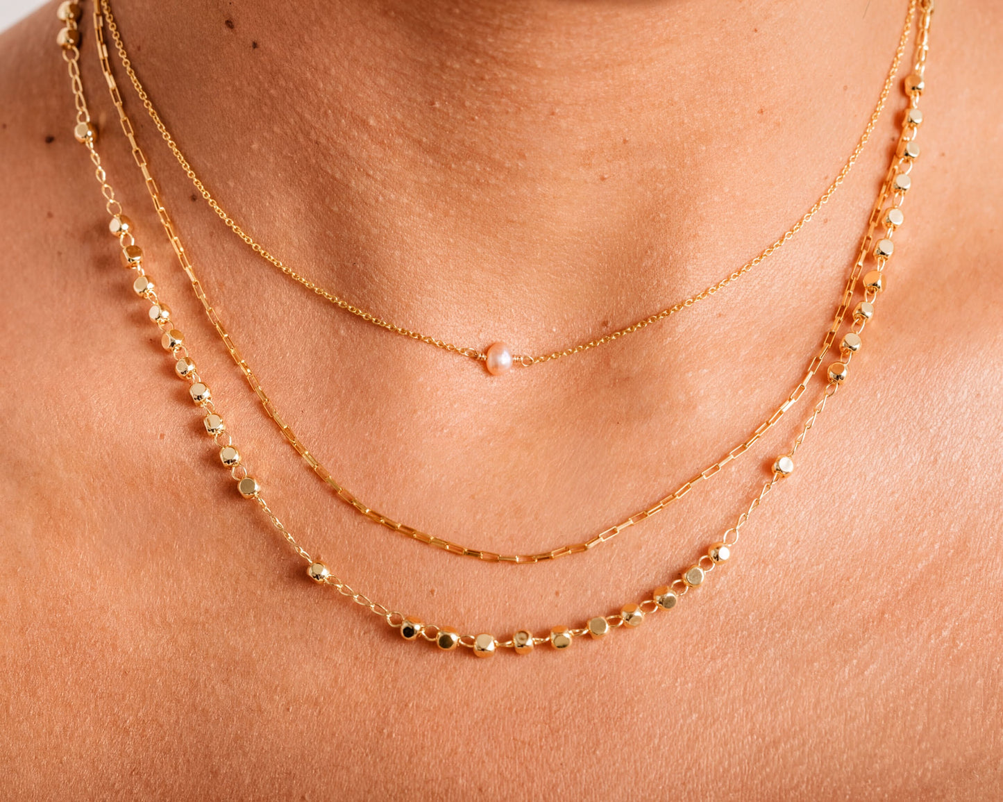 A close-up view of a person's neck adorned with multiple gold necklaces.