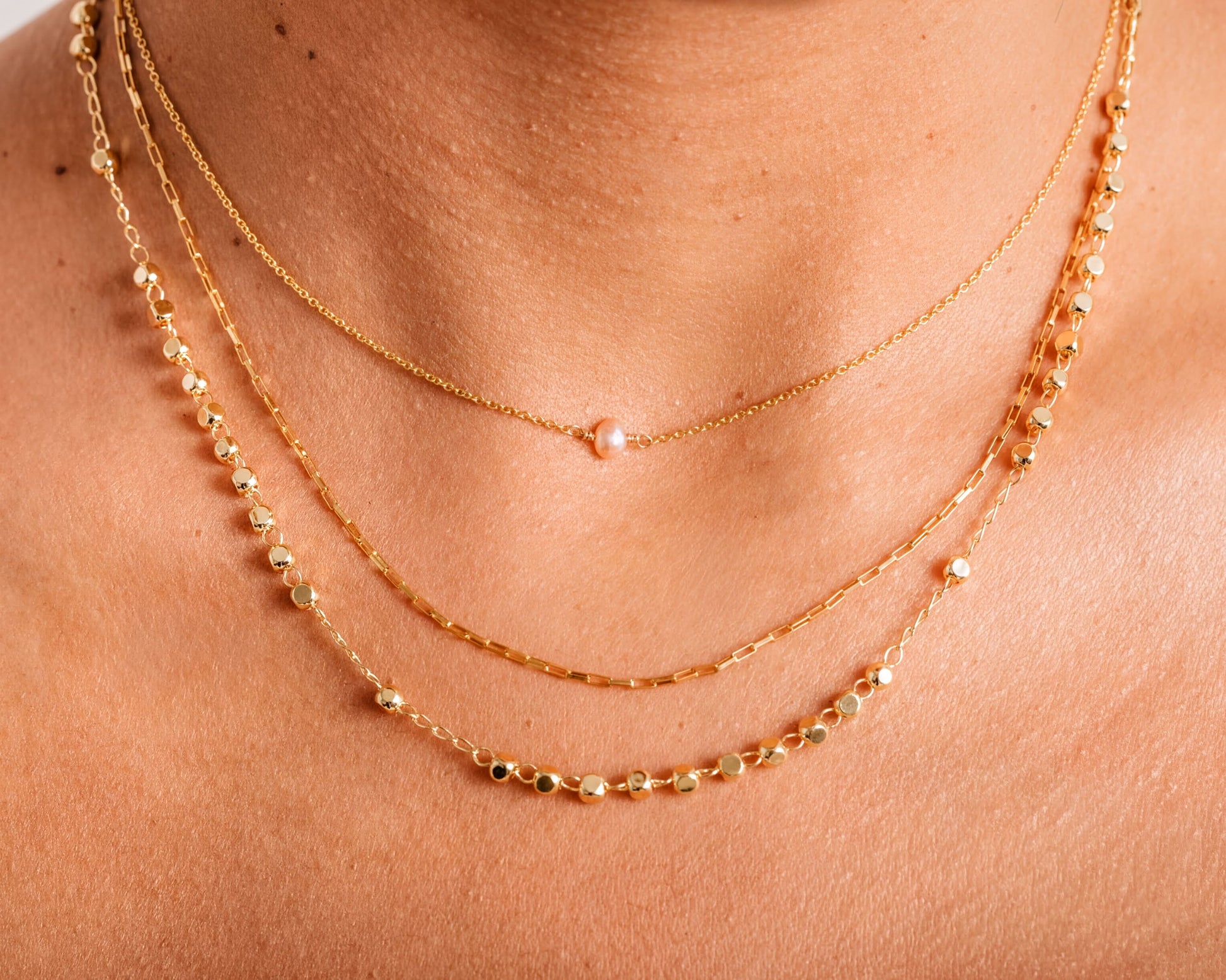 A close-up view of a person's neck adorned with multiple gold necklaces.