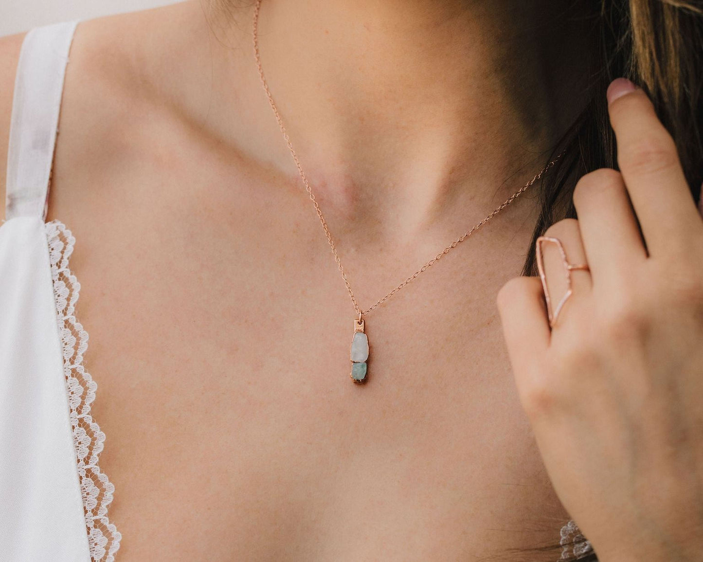 A close-up view of a woman's neck and chest area, featuring a delicate necklace with a pendant and a ring on her finger.