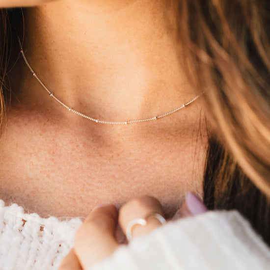 A close-up view of a person's neck and chest area, featuring a delicate necklace with small beads.