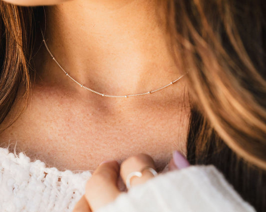 A close-up view of a person's neck and chest area, featuring a delicate necklace with small beads.