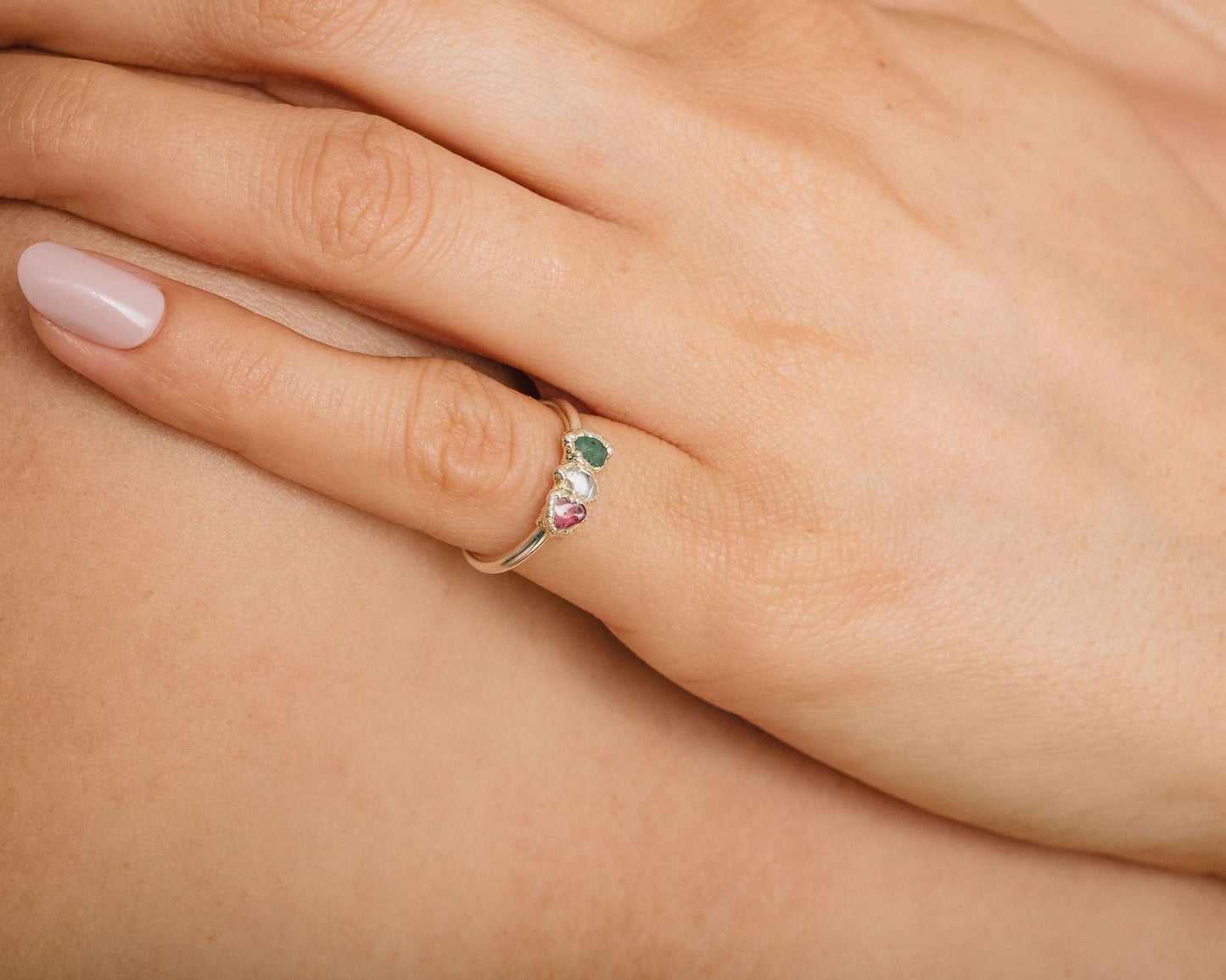 A close-up of a person's hand wearing a ring with three gemstones.