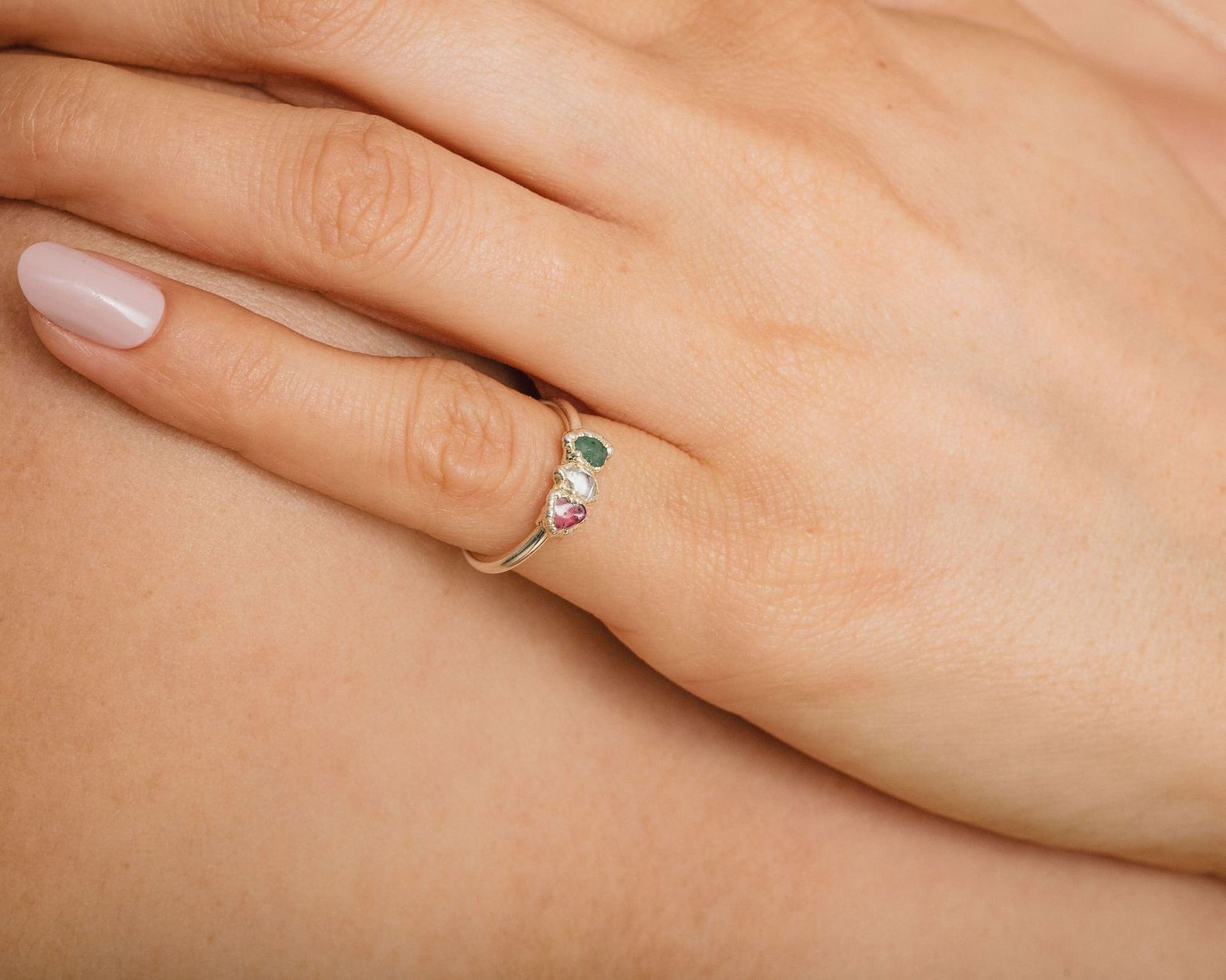 A close-up of a person's hand wearing a ring with three gemstones.