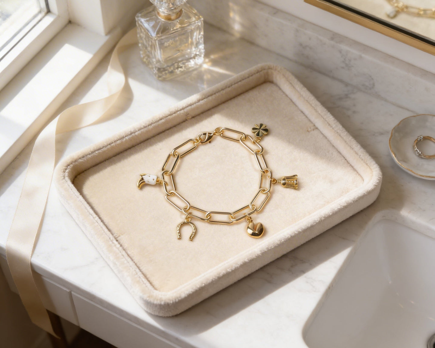 A gold-colored bracelet with charms is displayed on a white tray, placed on a bathroom counter.