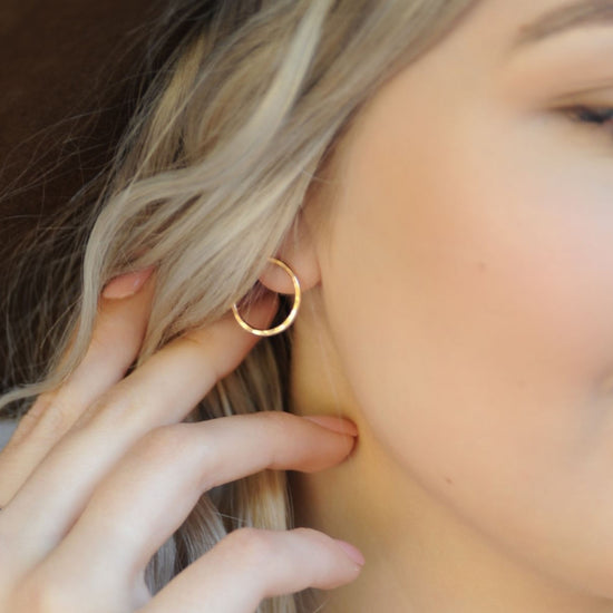 A close-up of a person's face, focusing on their earrings and fingers.
