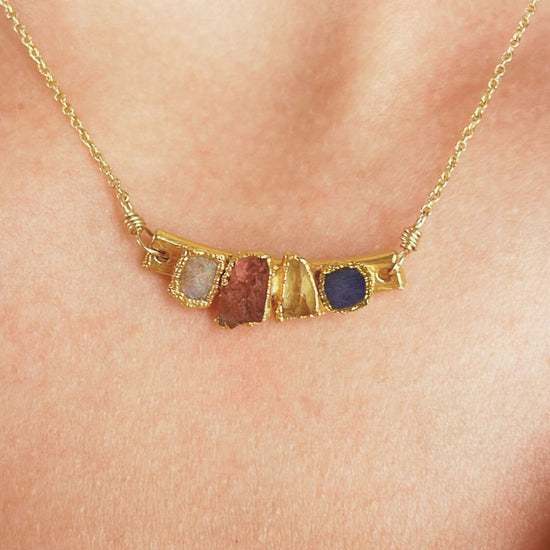 A gold necklace with a pendant featuring four different colored gemstones.