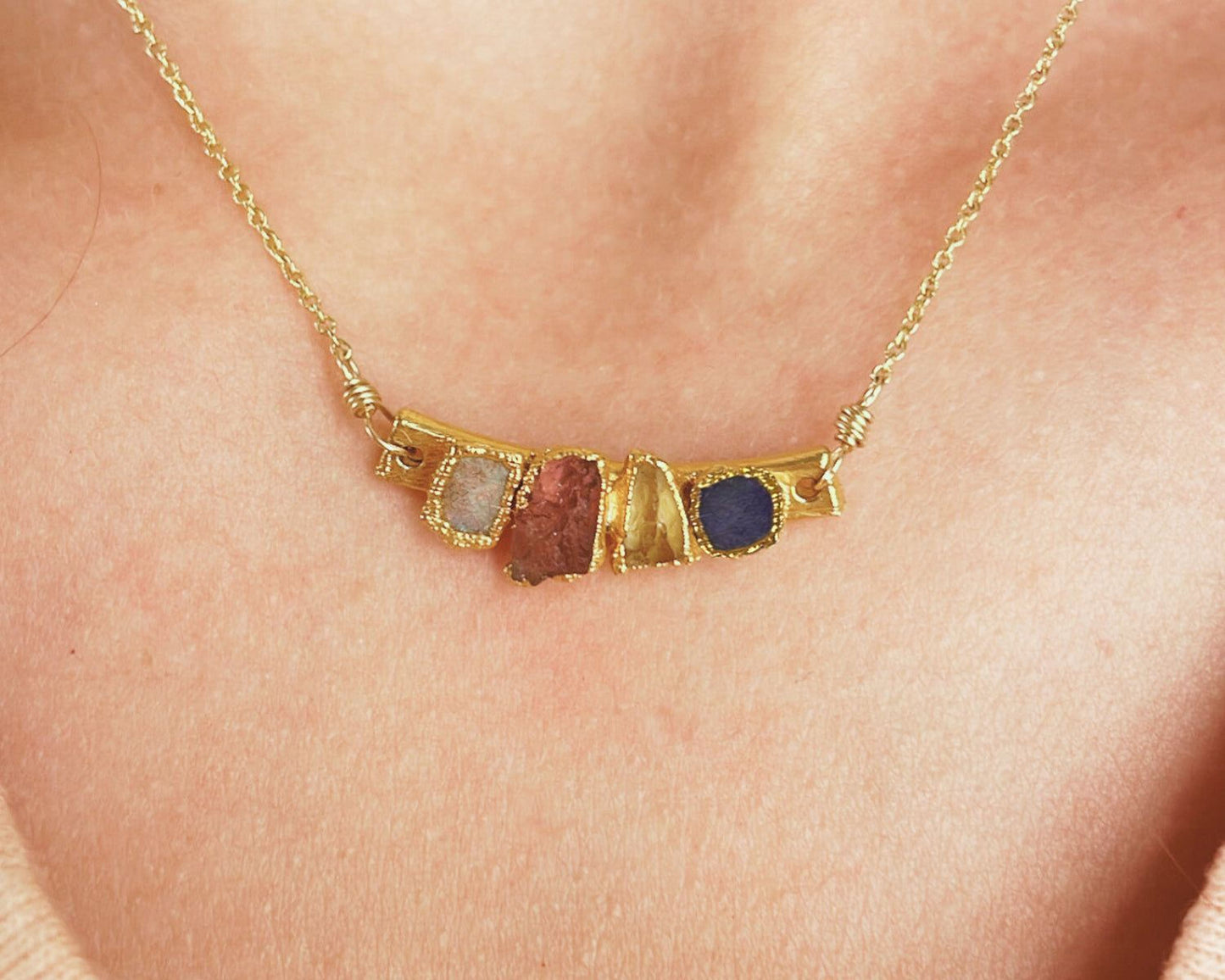 A gold necklace with a pendant featuring four different colored gemstones.