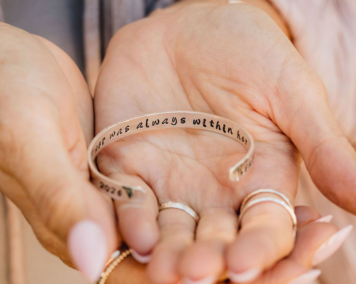 A person's hand holding a bracelet with the text "I always was always within here" engraved on it.