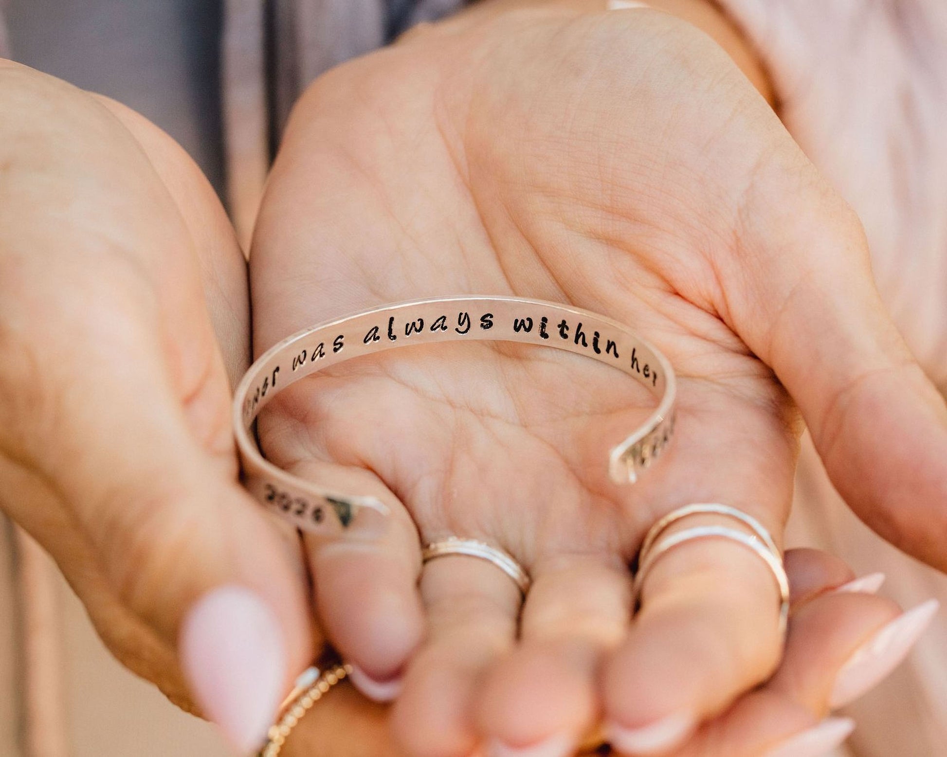 A person's hand holding a bracelet with the text "I always was always within here" engraved on it.