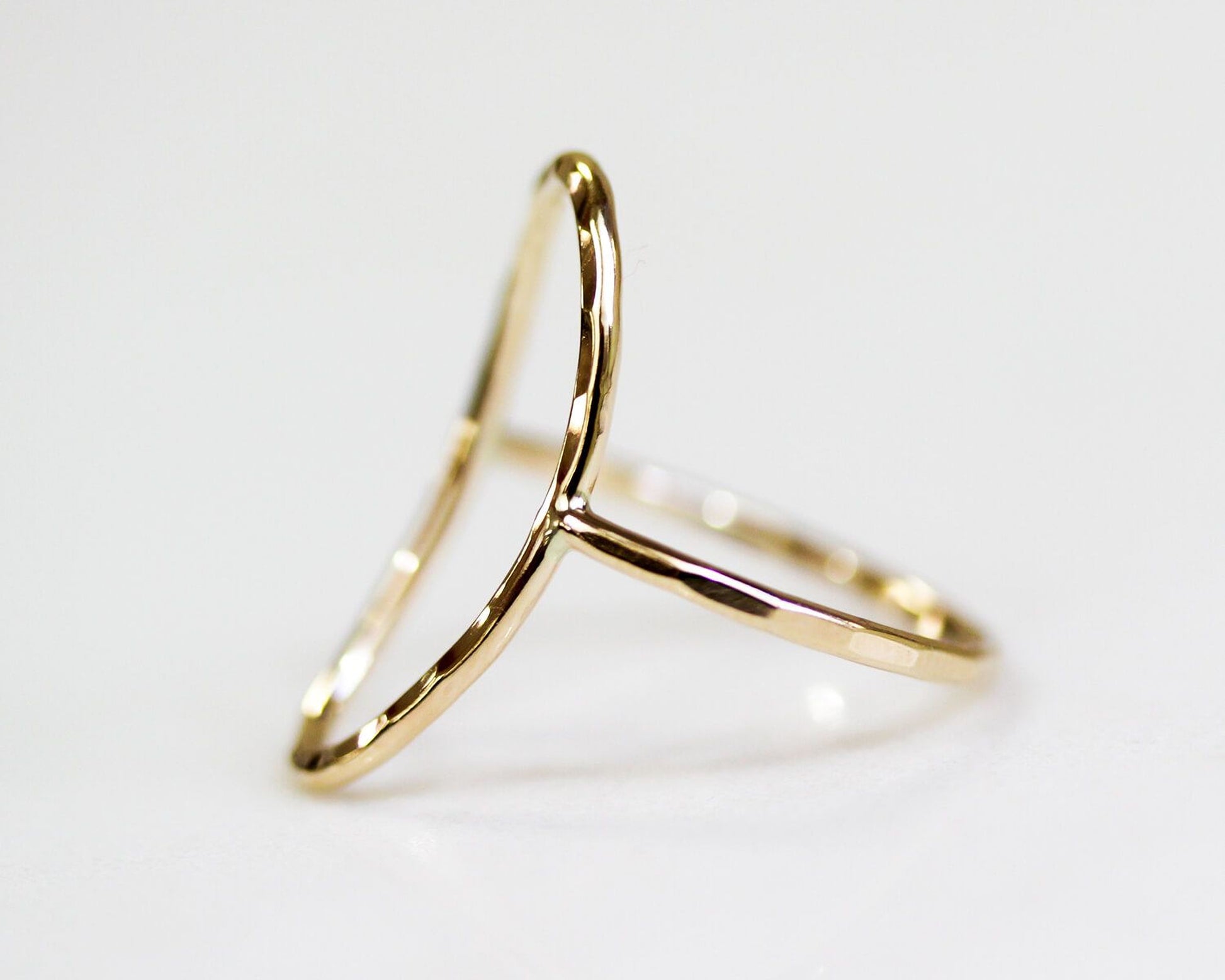 A gold ring with a unique, curved design sits on a white surface.