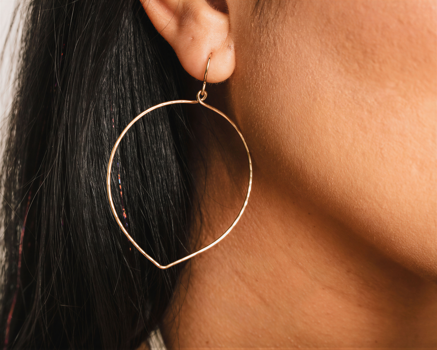 A close-up view of a person's ear wearing a gold hoop earring.