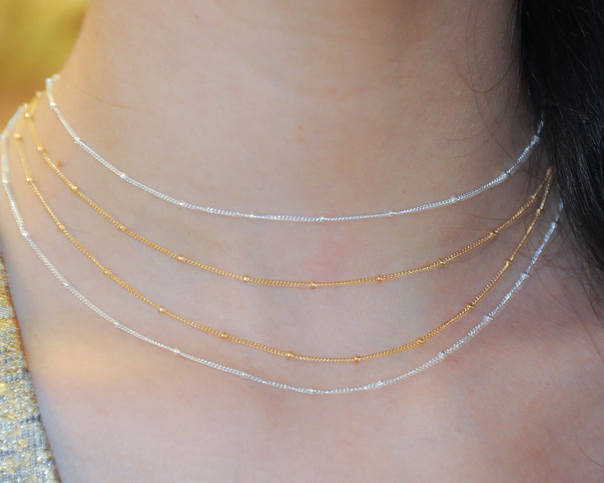 A close-up view of a person's neck adorned with a delicate necklace featuring three distinct strands of chain, each with a small, round bead.
