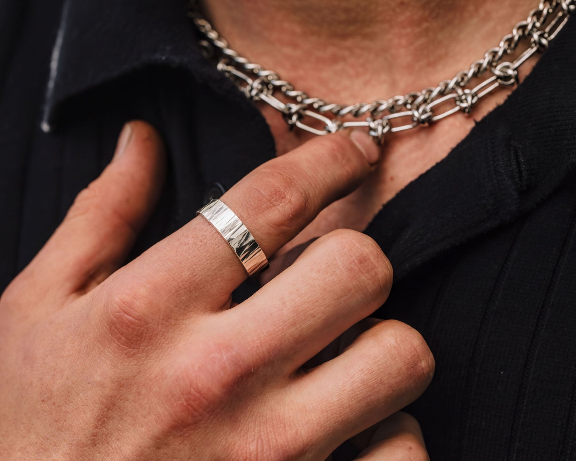 A close-up of a person's hand wearing a ring and a necklace, with the focus on the ring and the necklace.