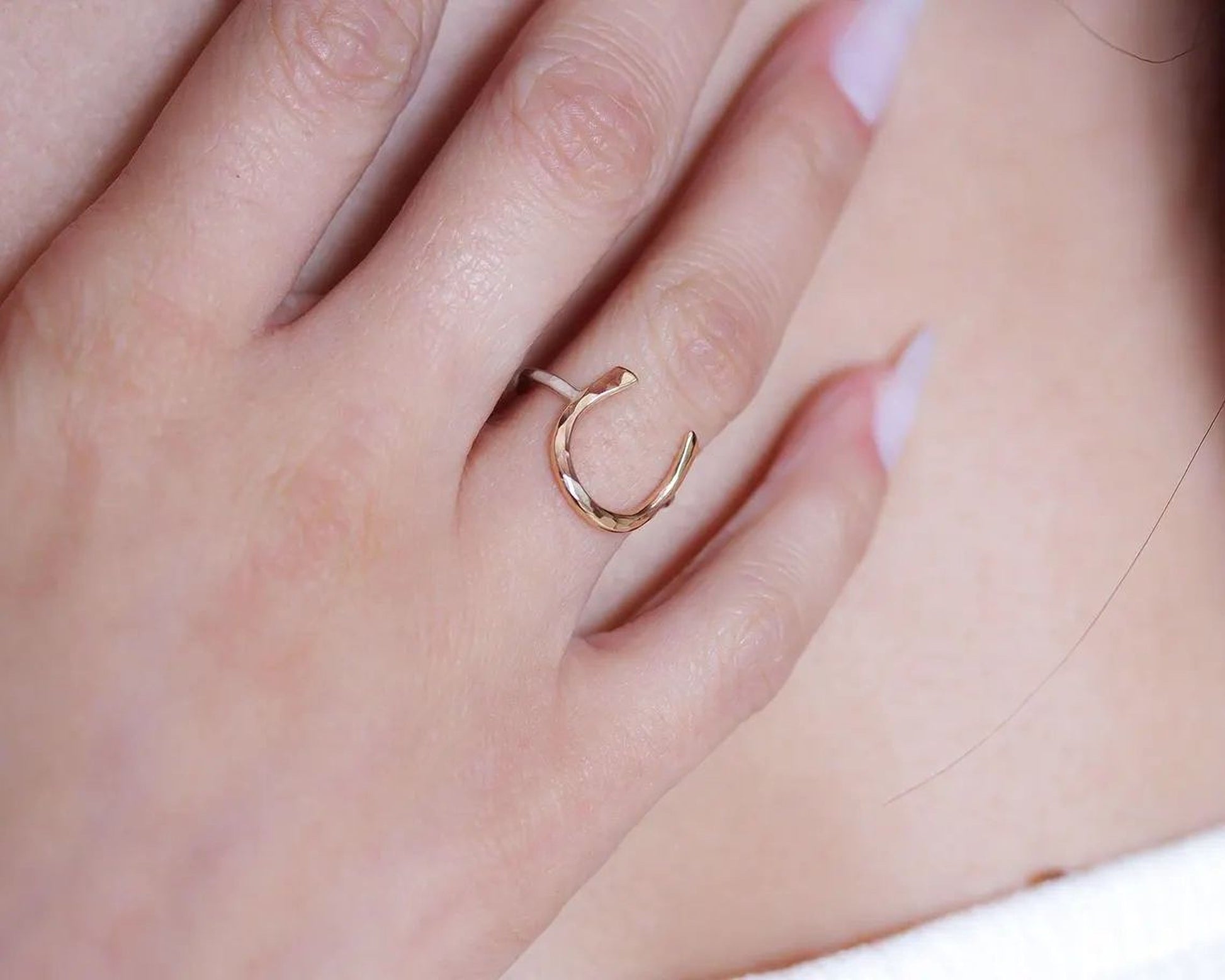A close-up of a person's hand wearing a gold ring with a horseshoe design.