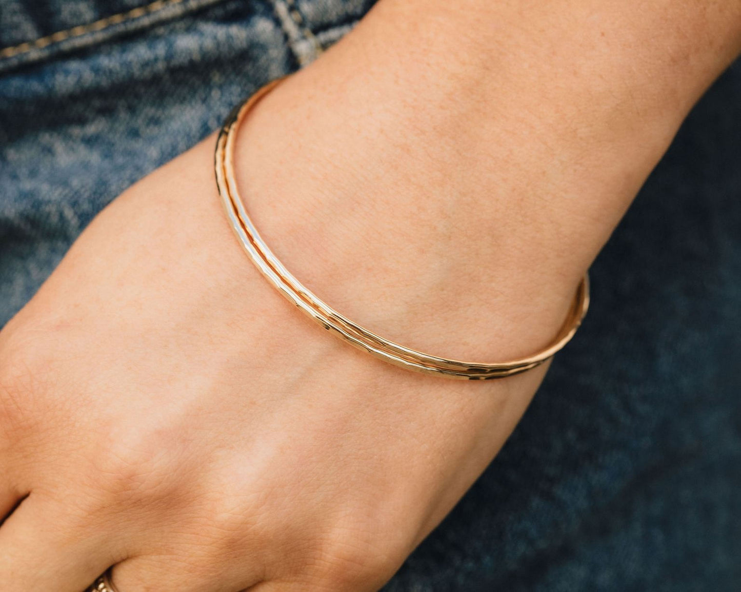 A gold-colored bangle bracelet is worn on a person's wrist.