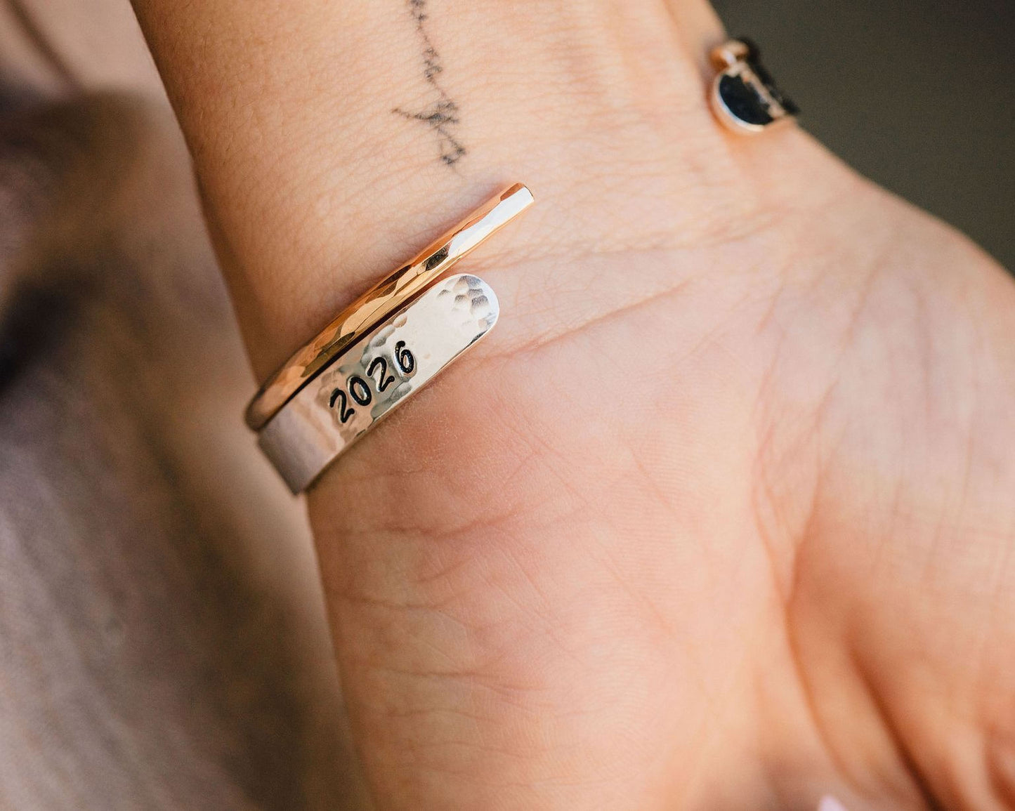 A close-up of a person's wrist wearing a silver bracelet with the year "2026" engraved on it.