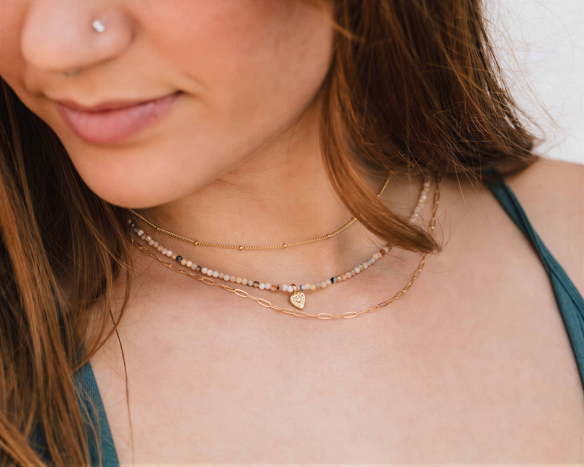 A close-up of a woman's face wearing multiple necklaces, including a beaded necklace and a chain necklace.
