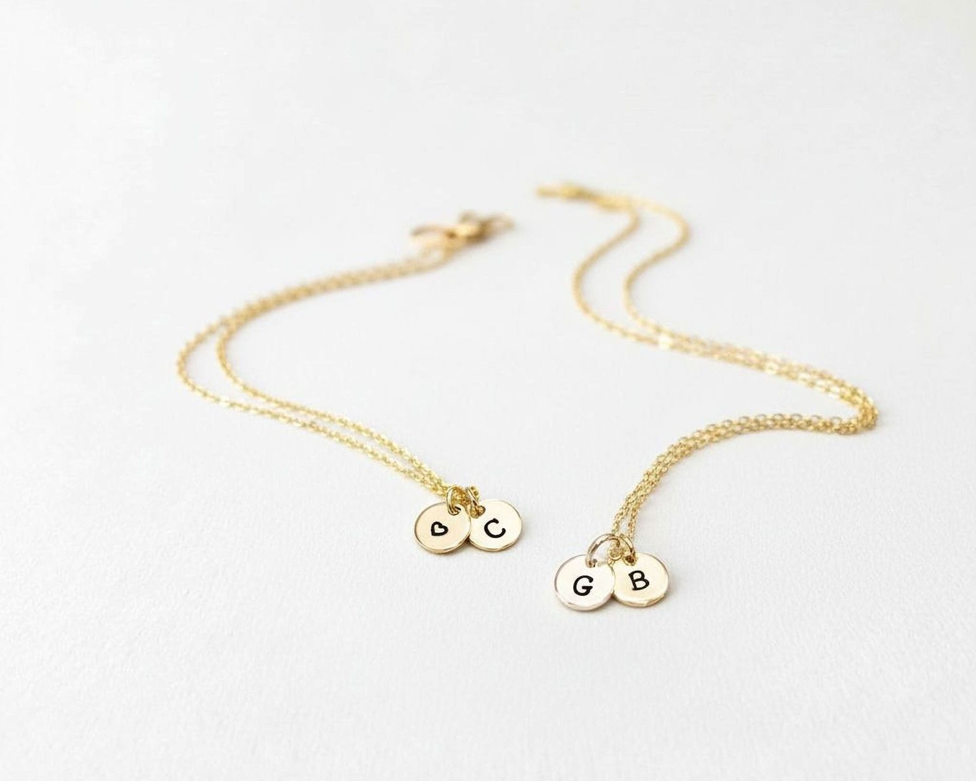 A pair of gold-colored necklaces with small charms attached, each containing a letter.