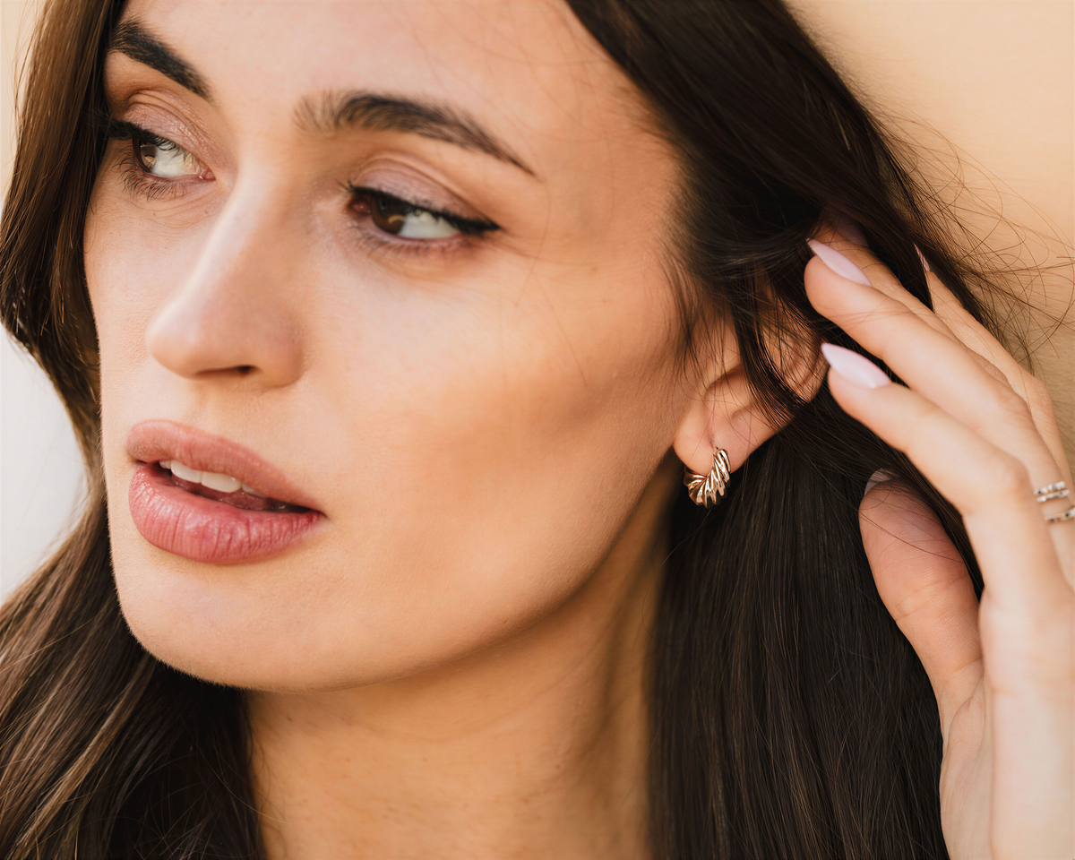 A close-up portrait of a woman with long dark hair, wearing a gold earring, and looking pensively at the camera.