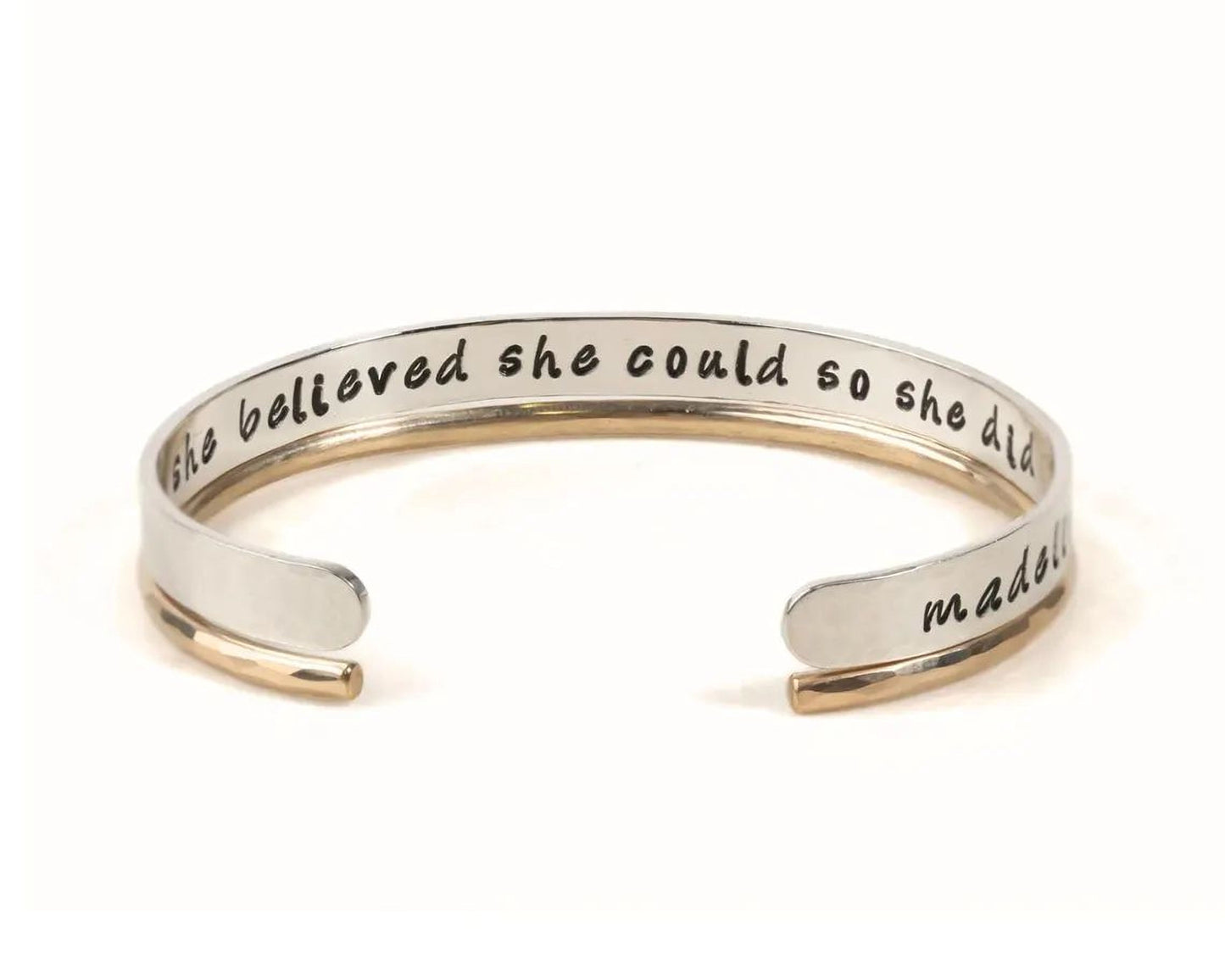 A silver and gold bracelet with the text "she believed she could so she did" engraved on it.