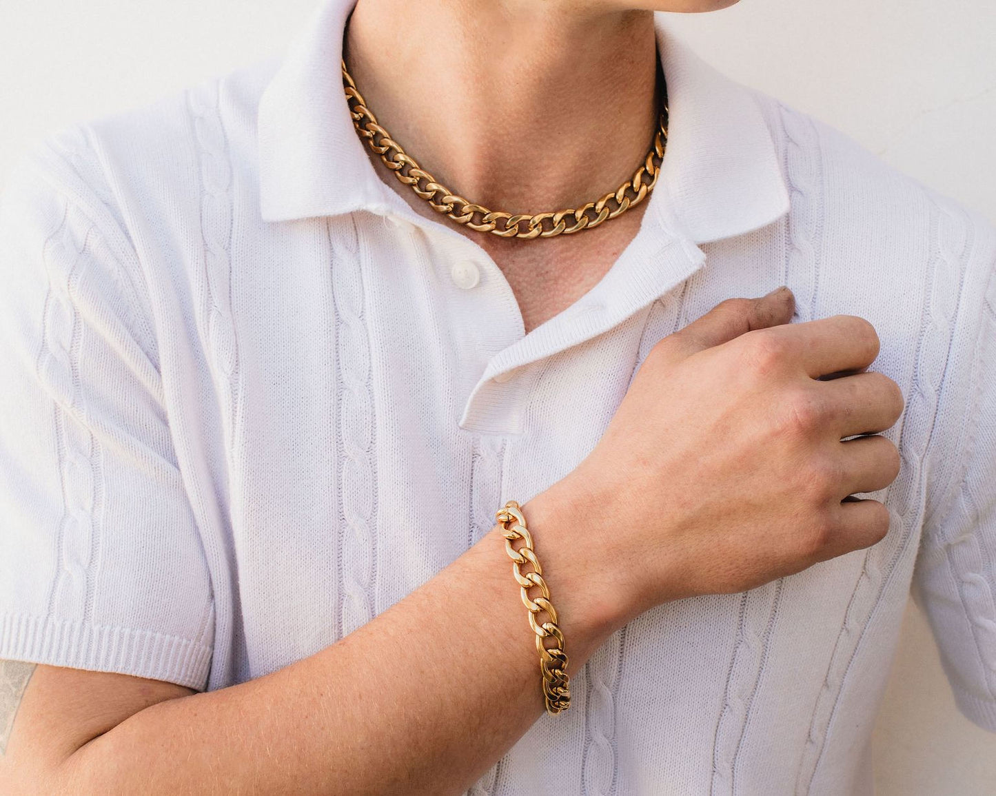 A close-up of a person wearing a white shirt and gold chain necklace and bracelet.