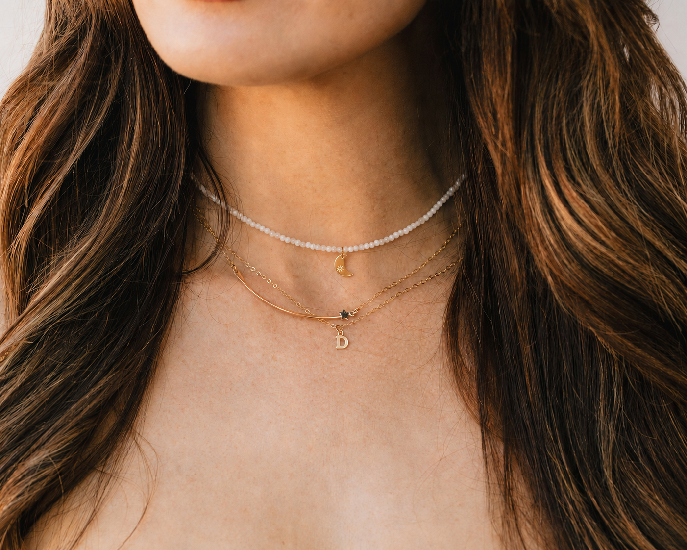 A close-up view of a woman's neck and chest area, showing a necklace with multiple pendants and a small charm.