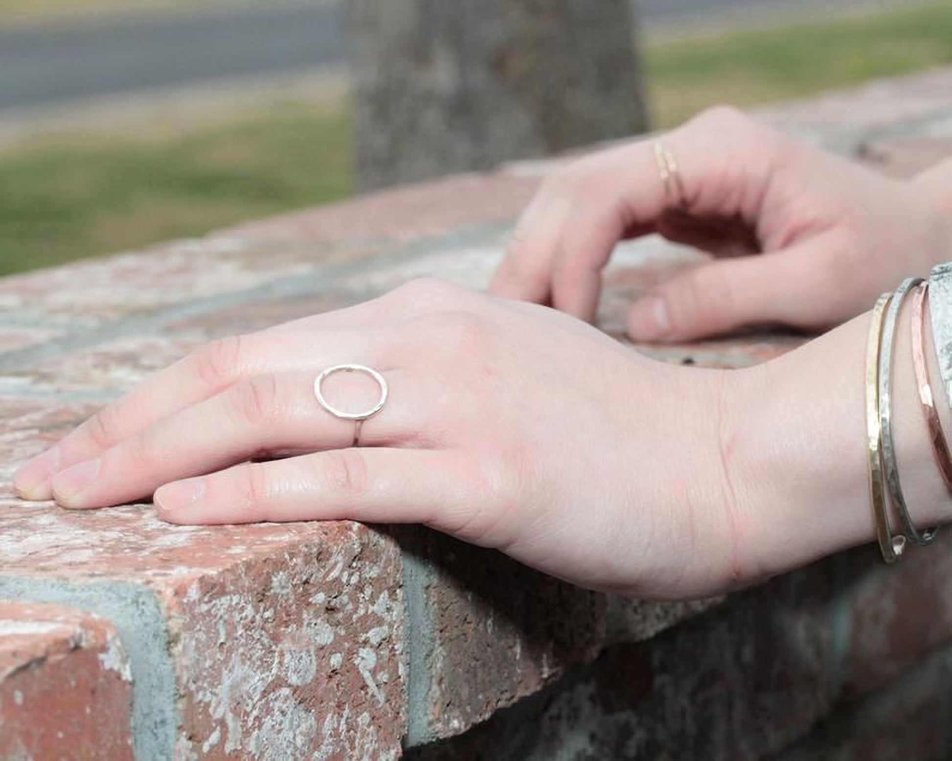A close-up view of a person's hand resting on a brick wall, wearing a ring and bracelets.