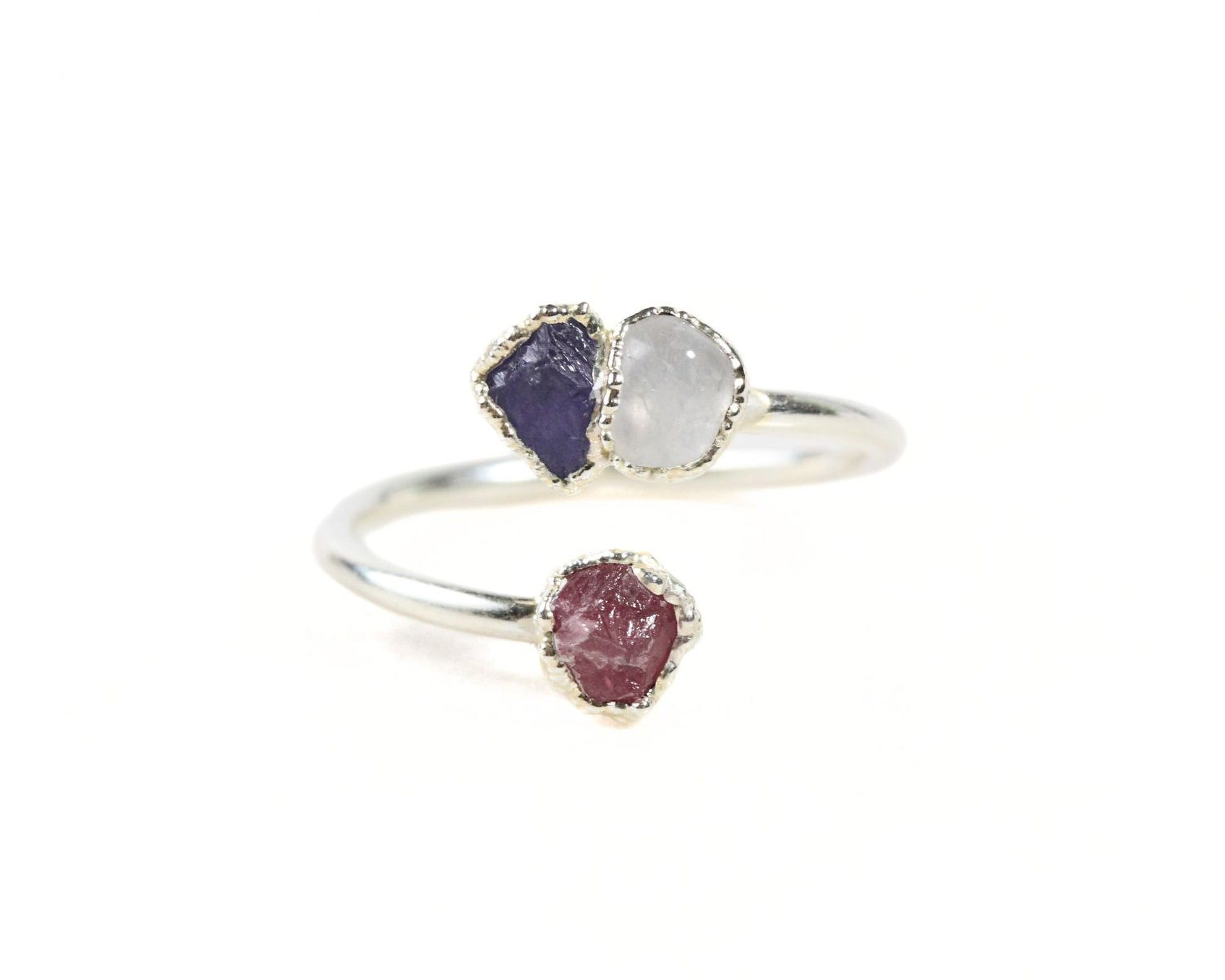 A silver ring with two gemstones, one purple and one white, set in a twisted design.