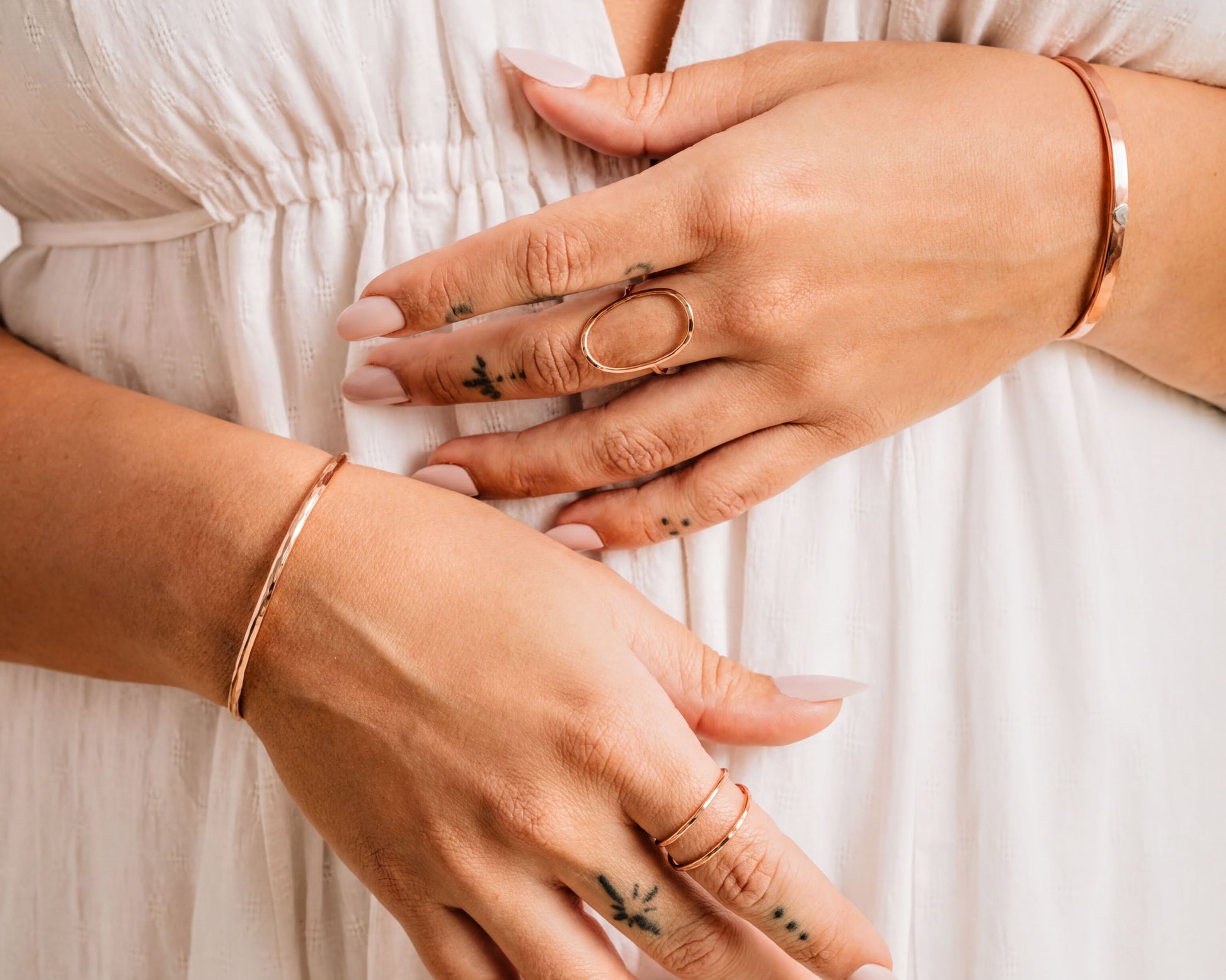 A close-up view of a person's hands wearing multiple rings and bracelets, with tattoos visible on their fingers.