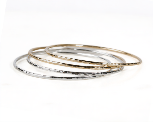 A stack of three silver and gold bangles on a white background.