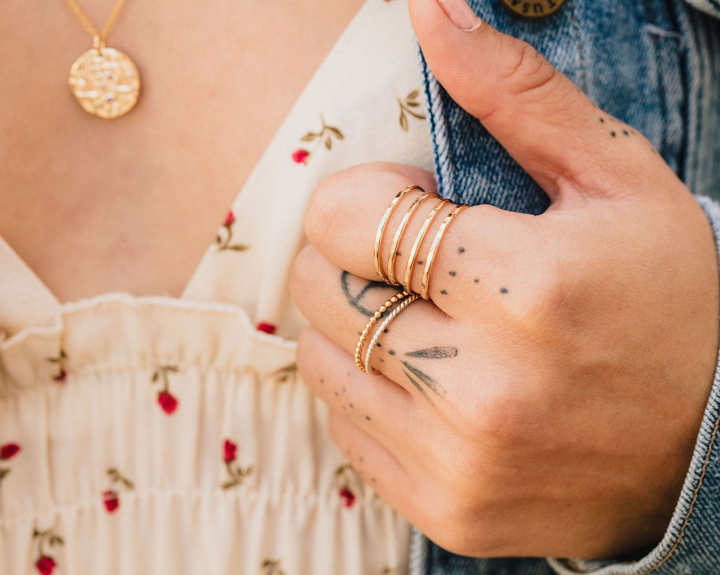 A close-up of a person's hand wearing multiple rings and a denim jacket.
