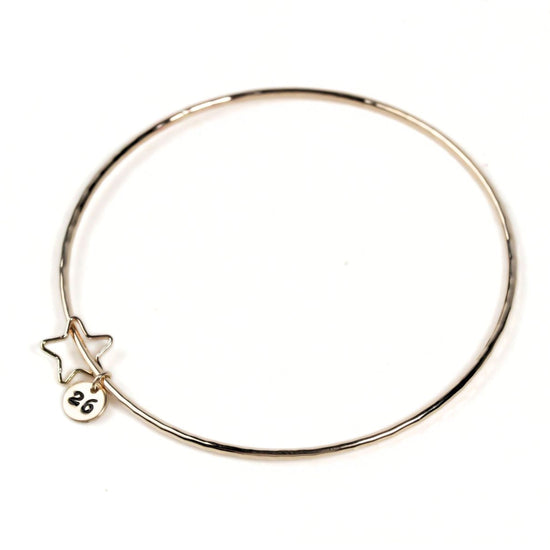 A gold-colored bangle bracelet with a small star charm attached to it.