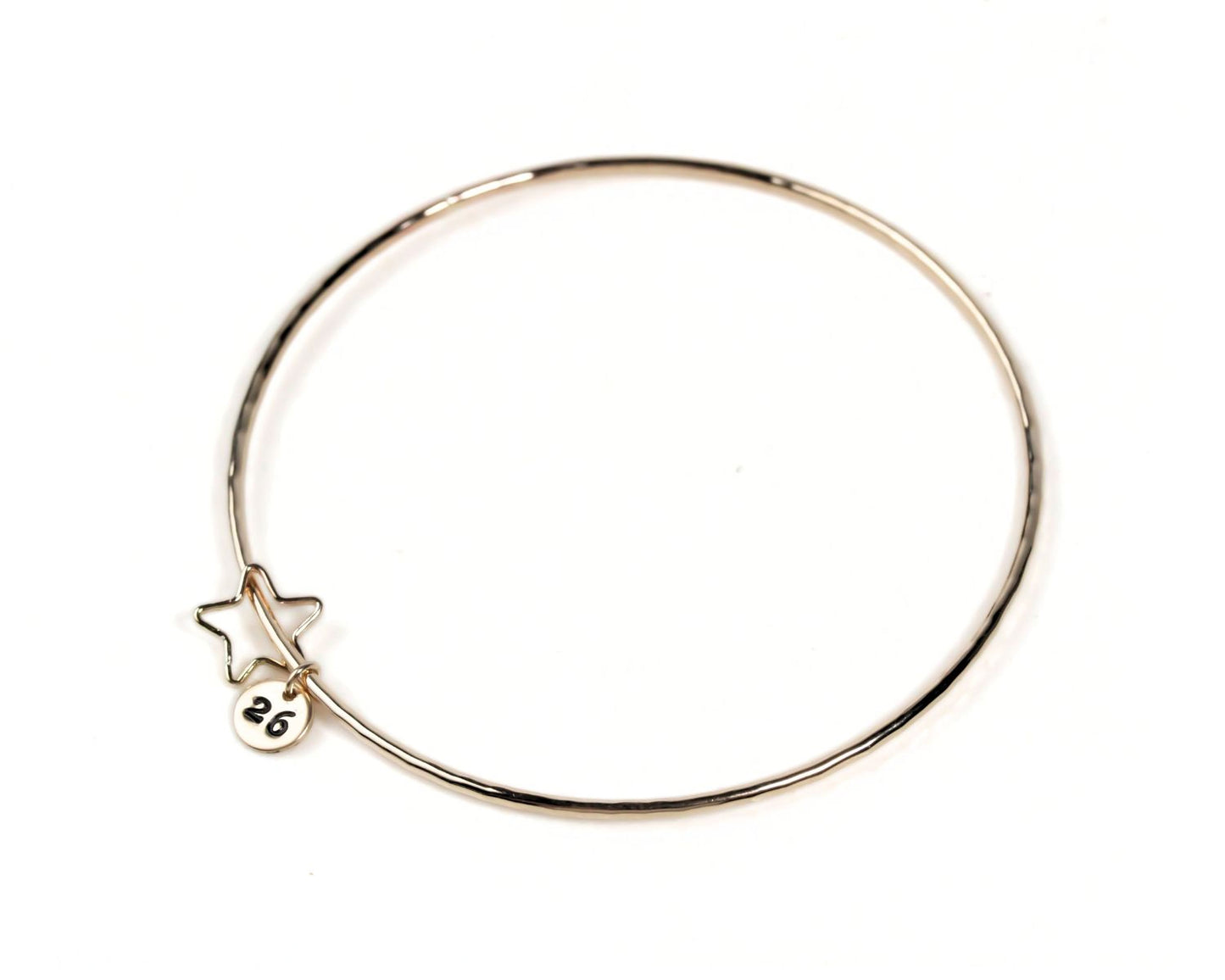 A gold-colored bangle bracelet with a small star charm attached to it.
