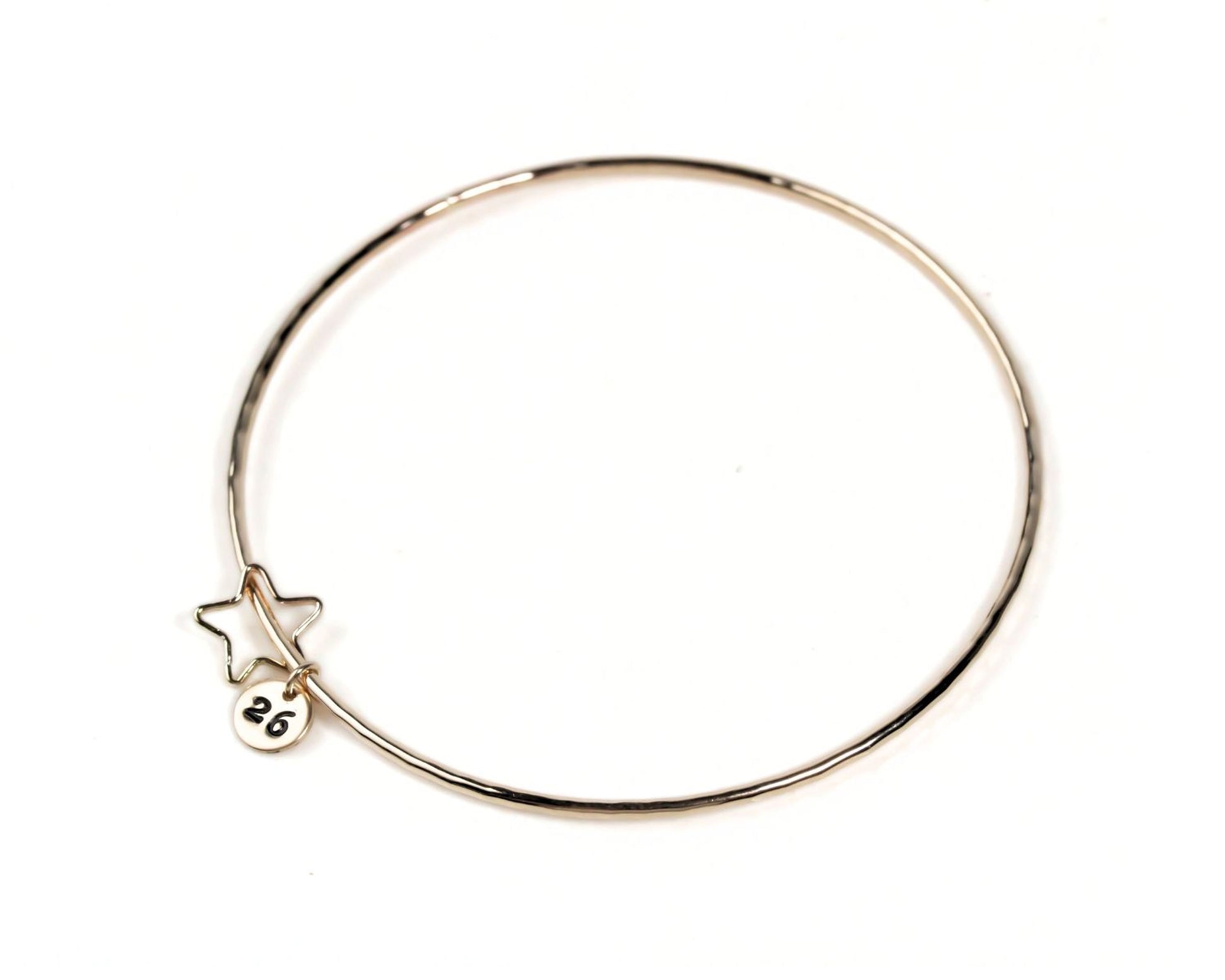 A gold-colored bangle bracelet with a small star charm attached to it.