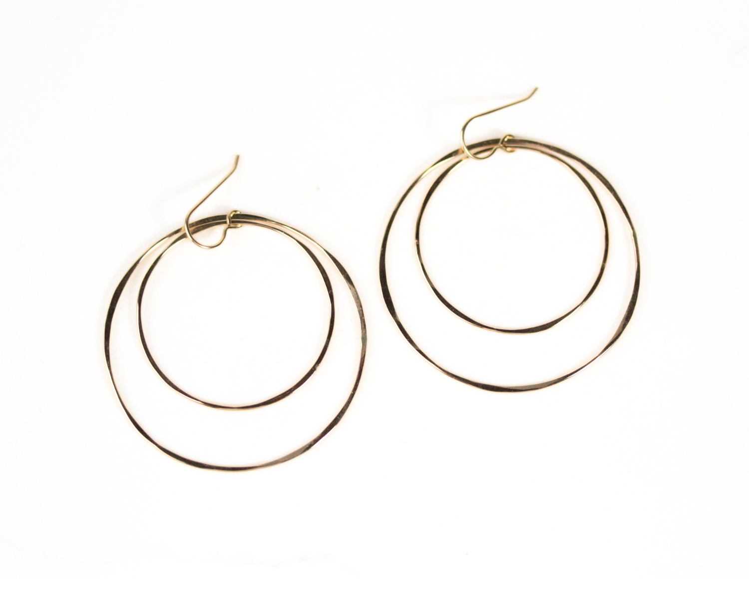 A pair of gold hoop earrings with a layered design, featuring two concentric circles connected by a thin gold hook.