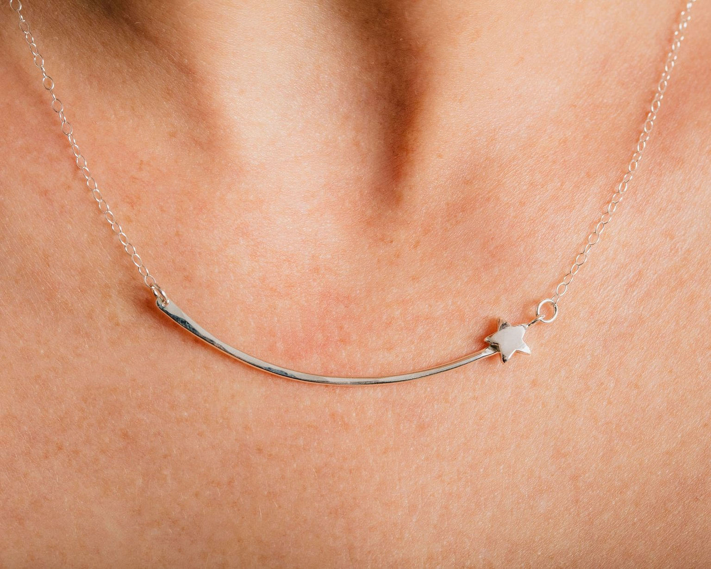 A close-up view of a silver necklace with a star-shaped charm on a curved metal bar.